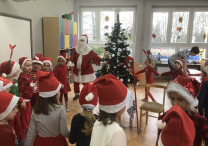 dzieci tańczą w kole z Mikołajem wokół choinki